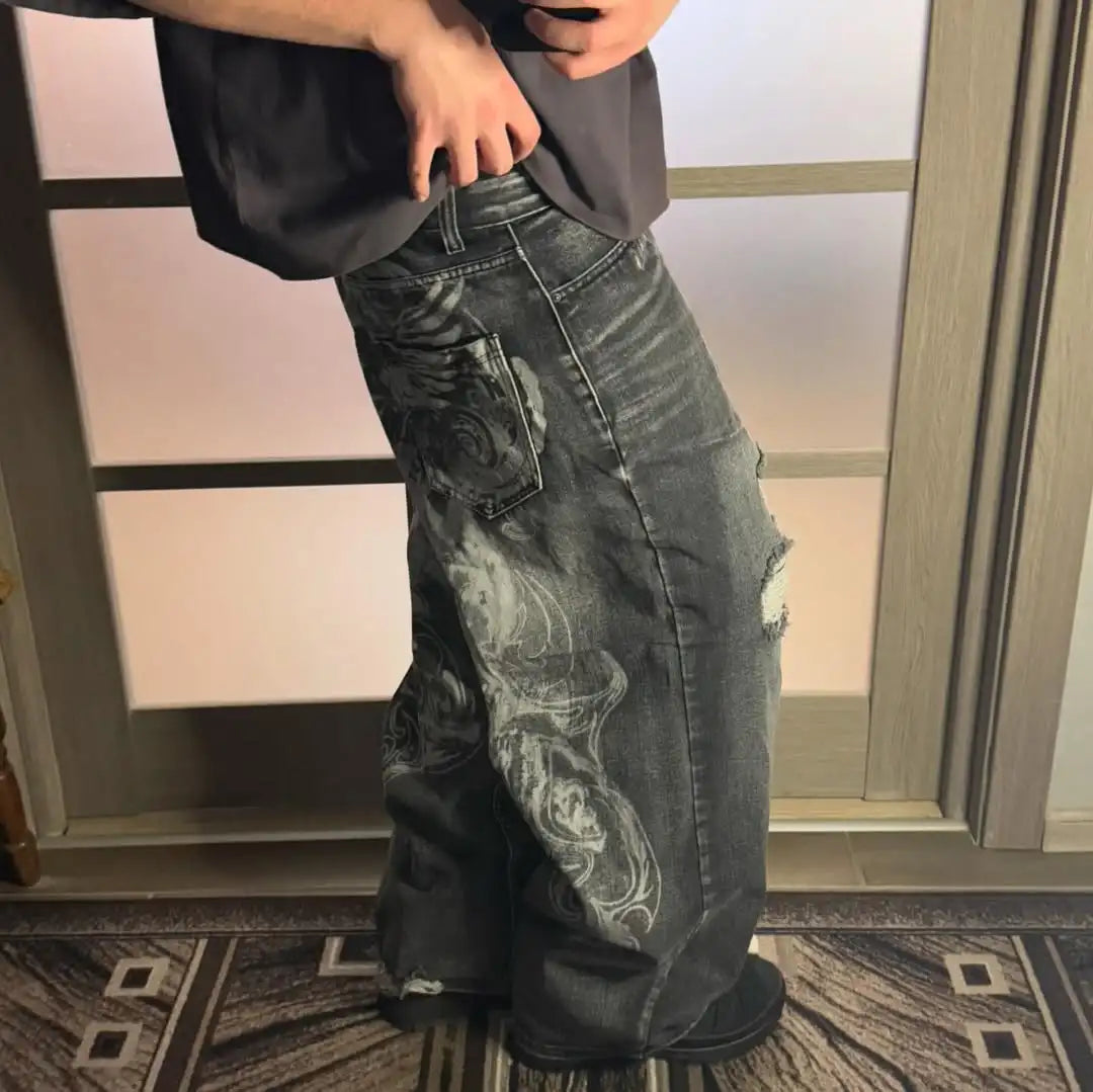 Person wearing a black t-shirt and distressed jeans standing indoors.
