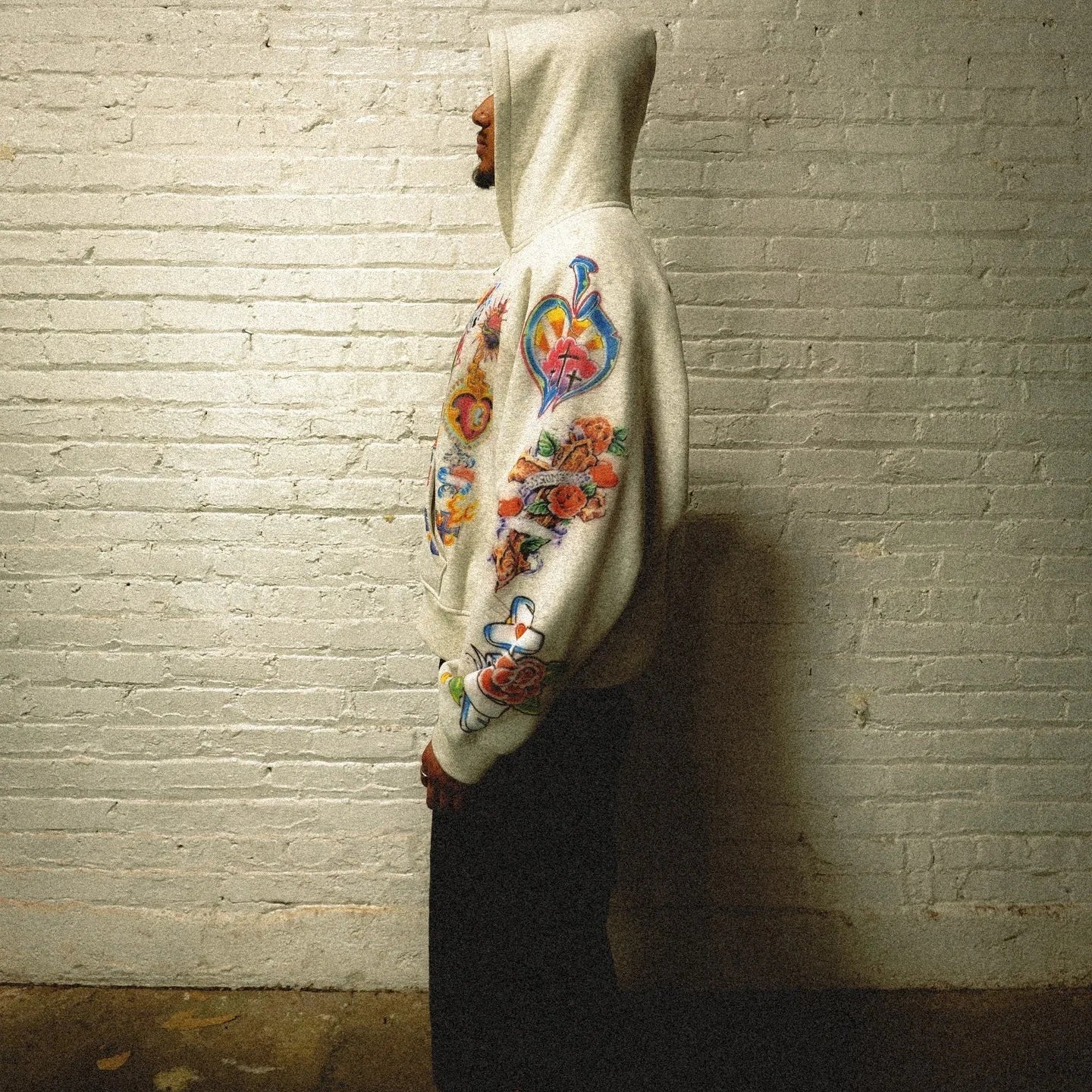Person wearing a white hoodie with colorful designs against a textured wall.