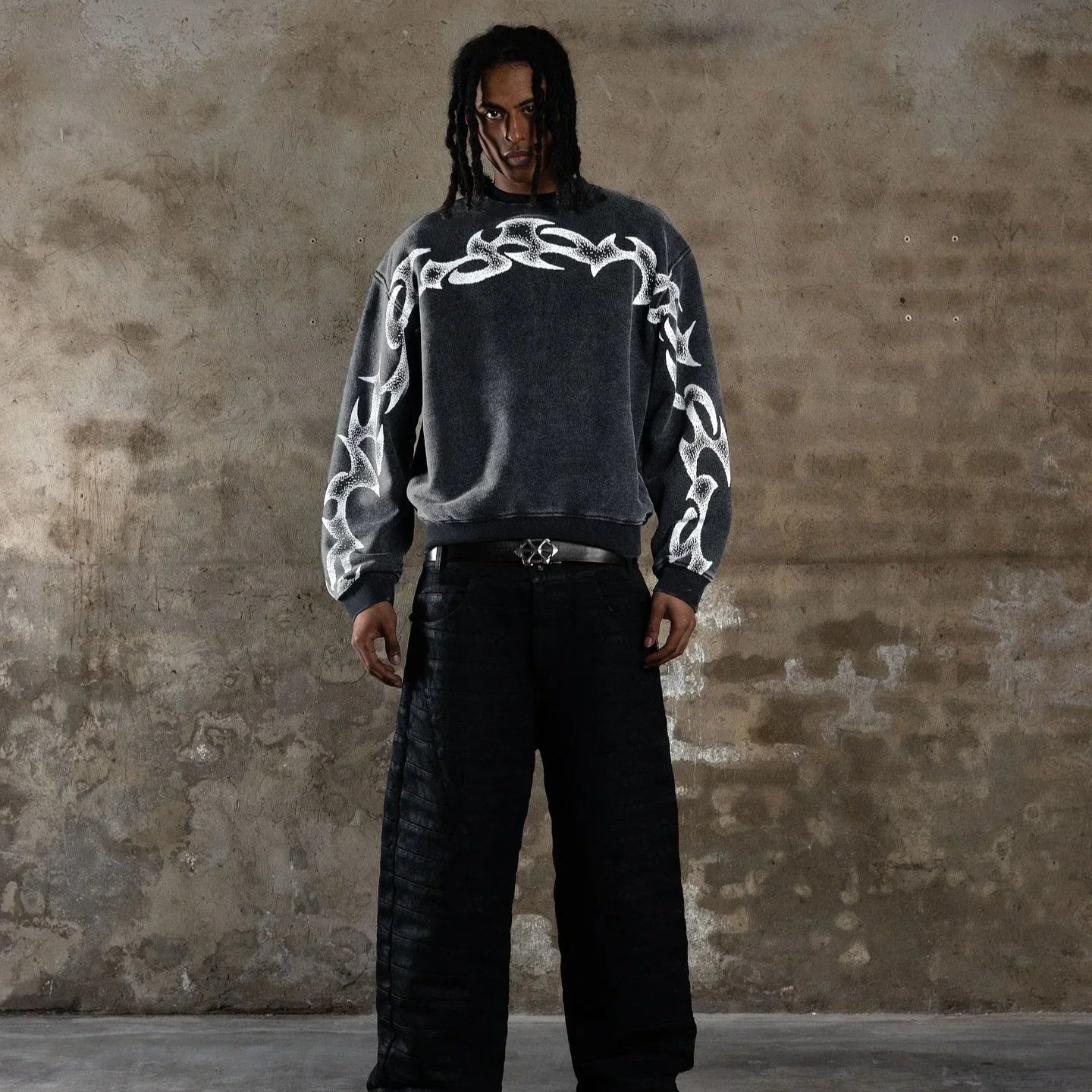 Person wearing a dark sweater with white patterns against a textured wall.