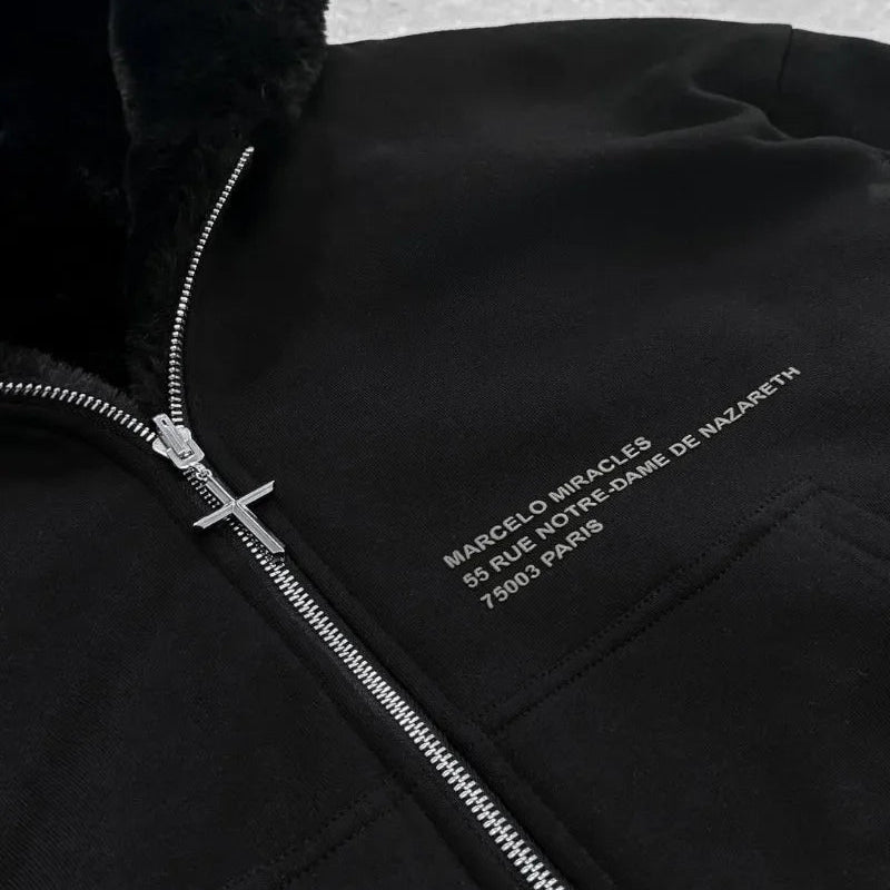 Black jacket with silver zipper and embroidered text on a textured gray background