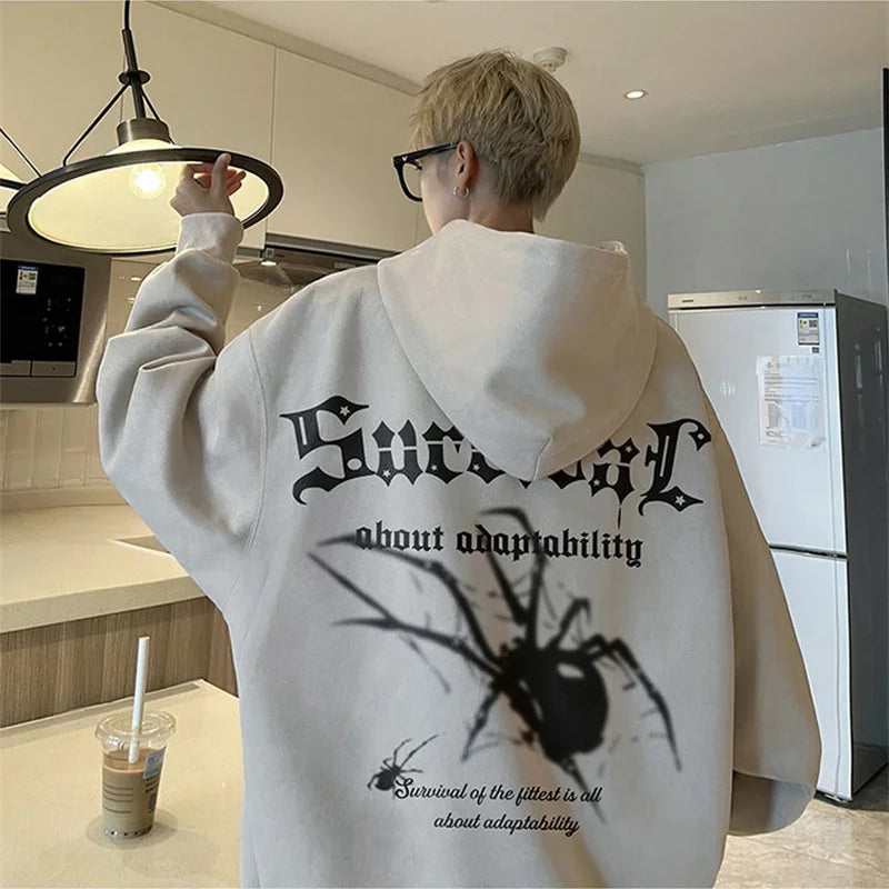 Person wearing a white hoodie with a spider graphic and text in a kitchen.