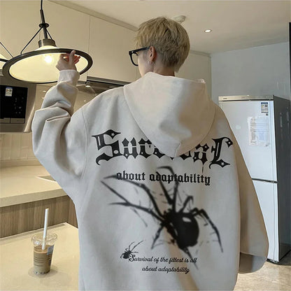 Person wearing a white hoodie with a spider graphic and text in a kitchen.