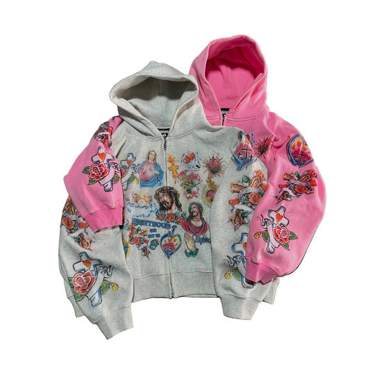 Two hoodies, one gray with colorful designs and one pink with floral patterns, on a concrete surface.