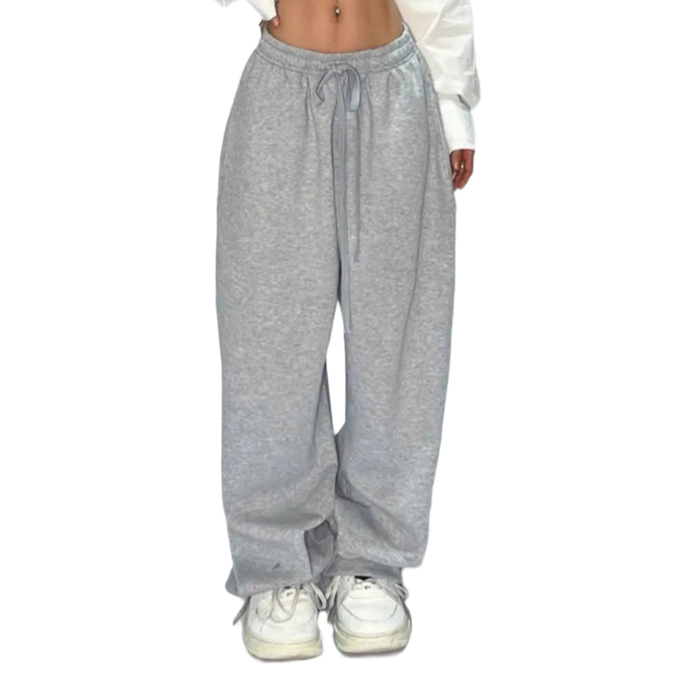 Person wearing a white cropped top and gray sweatpants on a plain background