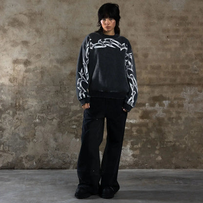 Person wearing a black sweater with white patterns against a textured wall.