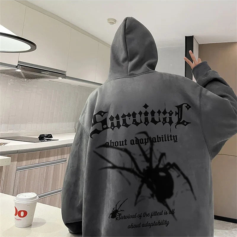 Person wearing a gray hoodie with a spider design and text in a kitchen.