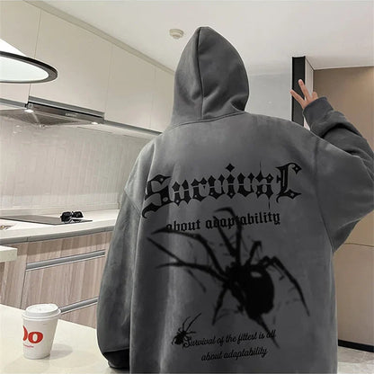 Person wearing a gray hoodie with a spider design and text in a kitchen.