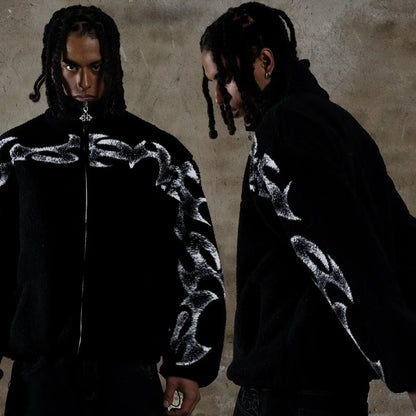 Person wearing a black jacket with chain design in front of a textured wall.