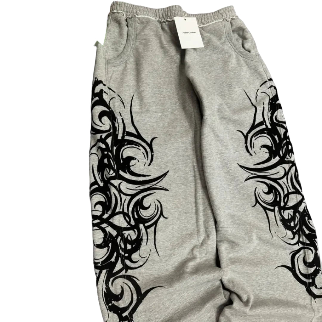 Gray sweatpants with black tribal designs on a gray surface.