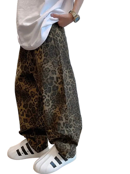 Person wearing leopard print pants and white Adidas shoes against a plain background