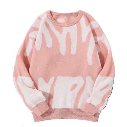 Pink sweater with white abstract patterns on a gray surface with white sneakers and sunglasses.